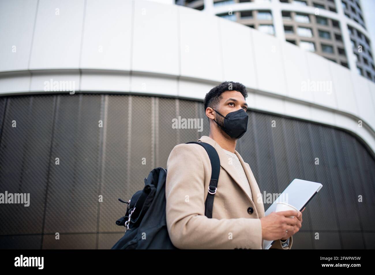 Glücklicher Mann mit Laptop auf dem Weg zur Arbeit im Freien in der Stadt, Coronavirus-Konzept. Stockfoto