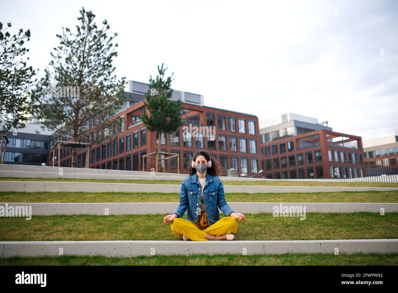 Frau mit Kopfhörern macht Yoga im Freien im Park in der Stadt, Coronavirus-Konzept. Stockfoto