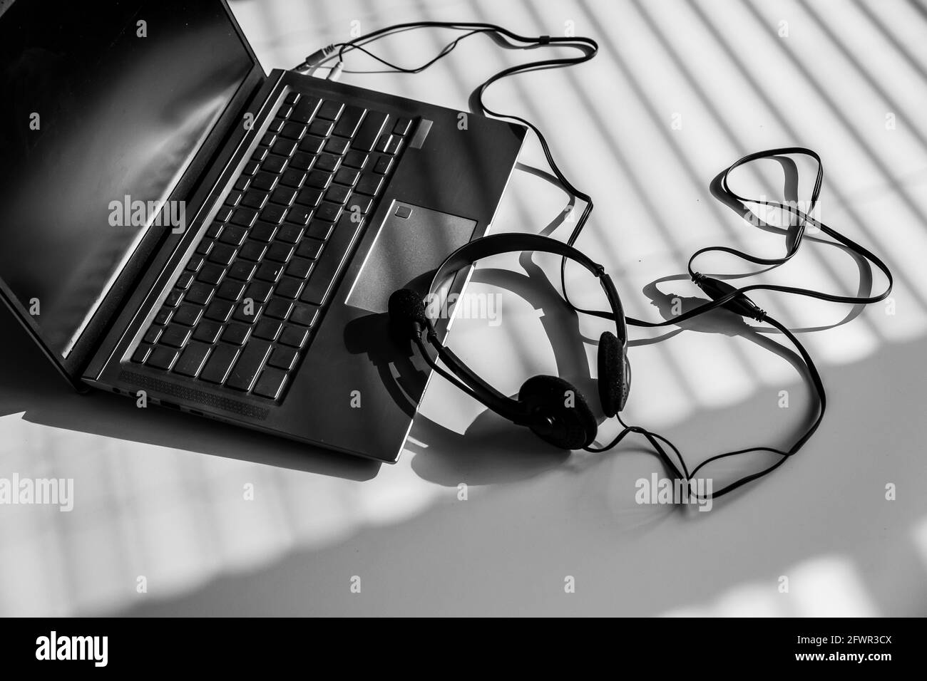 Draufsicht des Headsets auf dem Laptop im Schatten der Jalousien. Stockfoto