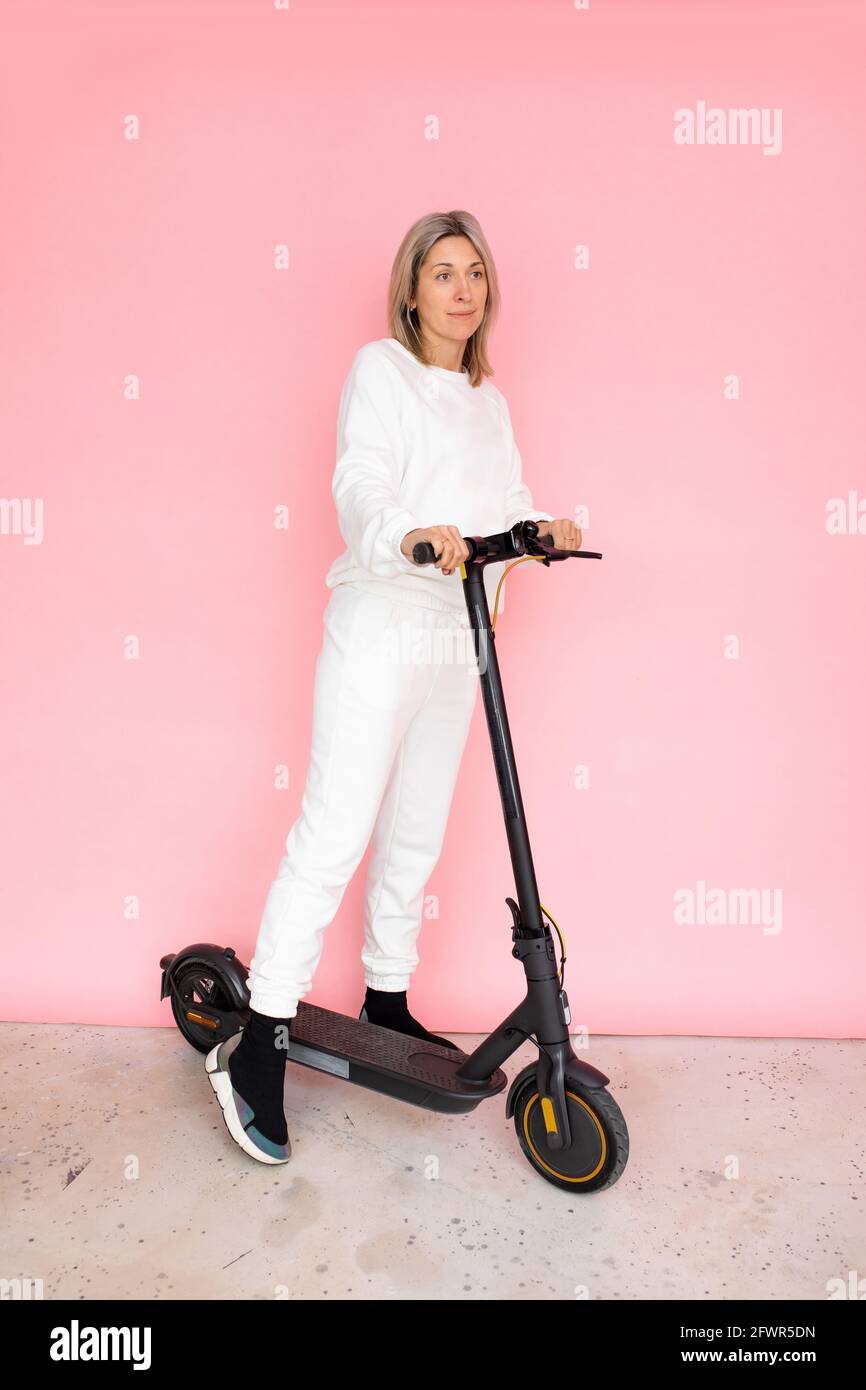 Eine Frau auf Elektrizität Push Scooter auf rosa Hintergrund, Studio Shot Stockfoto
