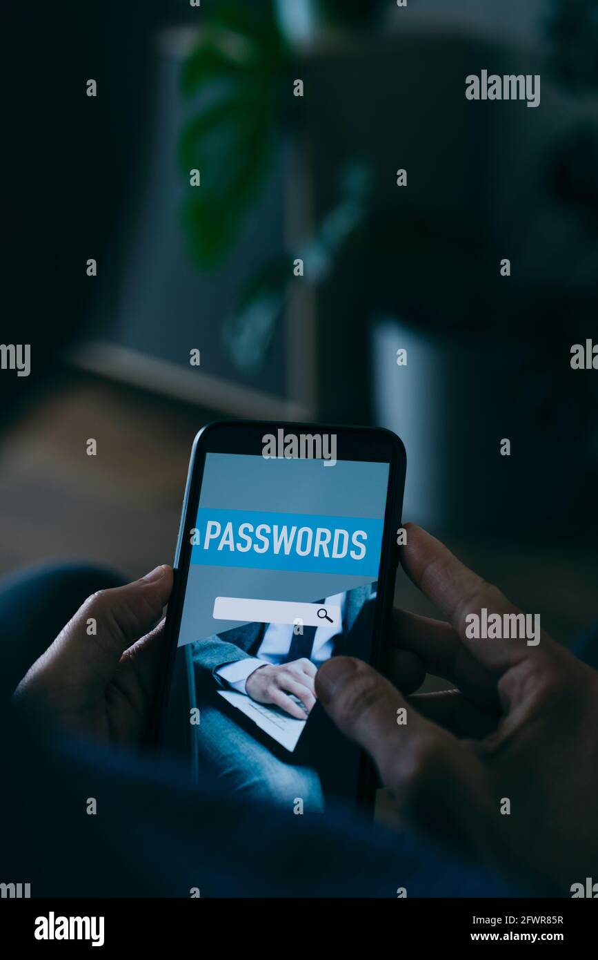 Nahaufnahme eines jungen kaukasischen Mannes zu Hause, der einen Passwort-Manager in seinem Smartphone verwendet, mit einer simulierten Passwort-Manager-App auf dem Bildschirm Stockfoto