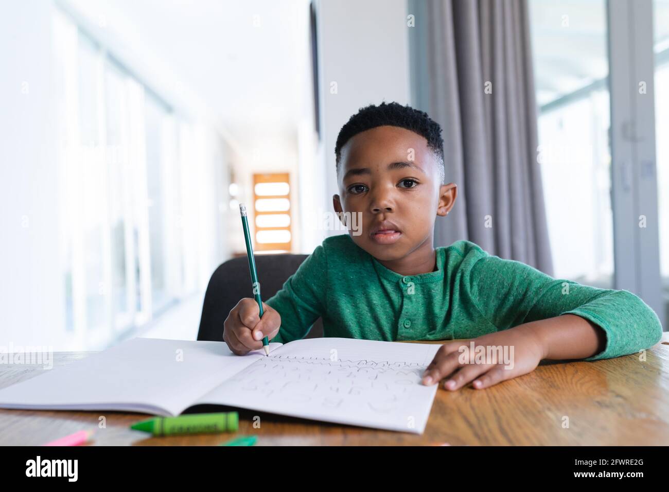 afroamerikanischer Junge in der Online-Schulklasse, der in seinem Notizbuch schreibt Stockfoto