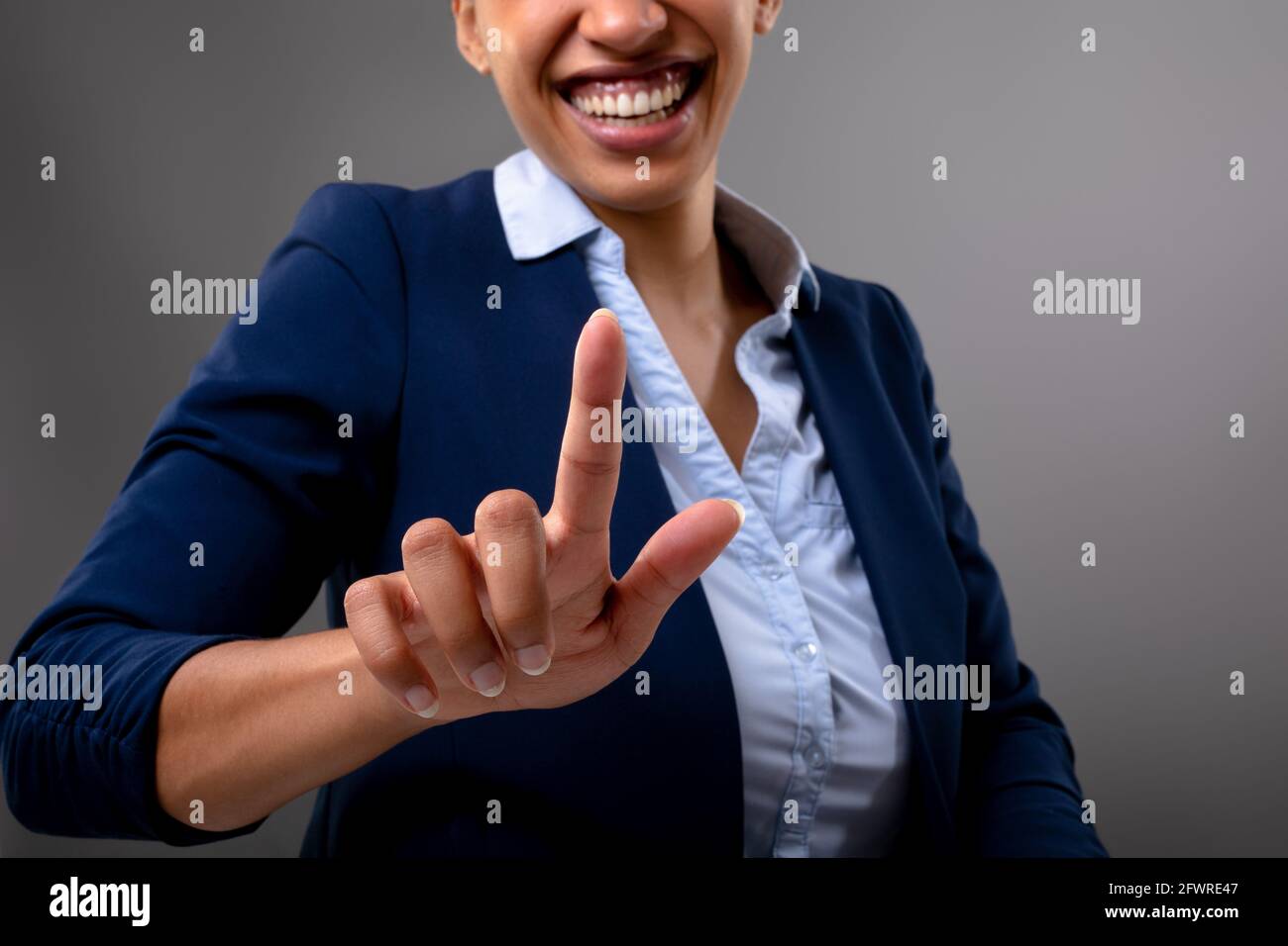 Mittelteil der afroamerikanischen Geschäftsfrau, die den unsichtbaren Bildschirm berührt Grauer Hintergrund Stockfoto