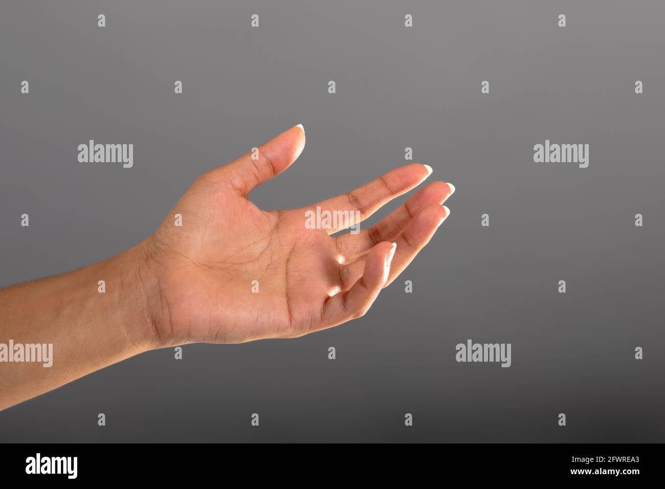 Nahaufnahme der Hand, die ein unsichtbares Objekt gegen Grau hält Hintergrund Stockfoto