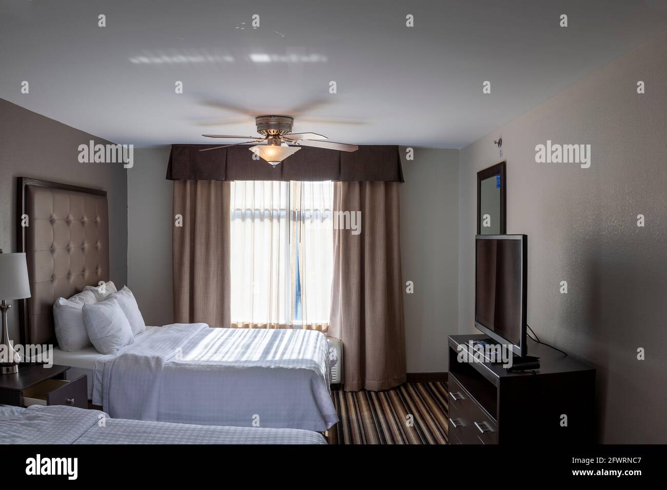 Pastellfarbene, moderne Hotelzimmer mit Flachbildfernseher auf einem Ständer mit Kommode und Teppichboden. Ein generisches Innenbild, bei dem die Sonne Stockfoto