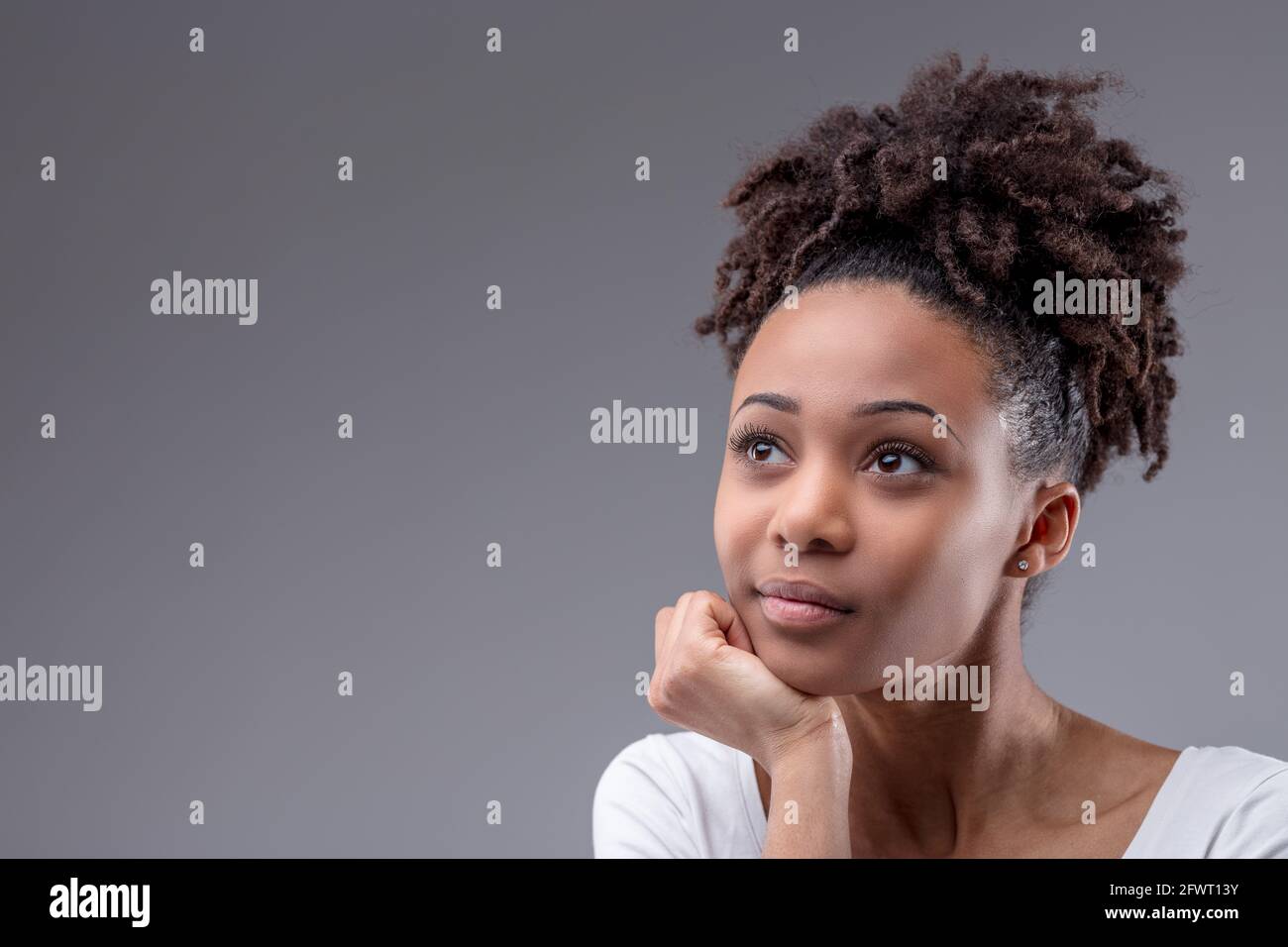 Ernsthafte junge schwarze Frau sitzt tief mit ihrem Kinn denkend Auf ihrer Hand ruhend und ein weit entfernender Ausdruck auf einem Grauer Studiohintergrund mit Copyac Stockfoto