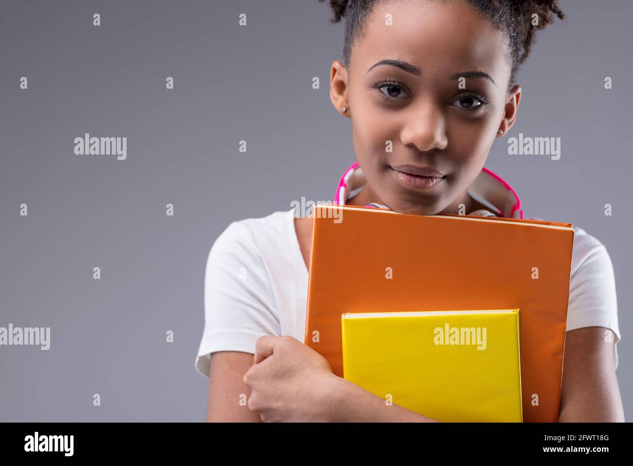 Ernst verantwortlich junge schwarze weibliche Studentin klammernden ihre Bücher als Sie blickt aufmerksam in Nahaufnahme auf die Kamera Beschnittenes Porträt auf einem grauen Studio Stockfoto