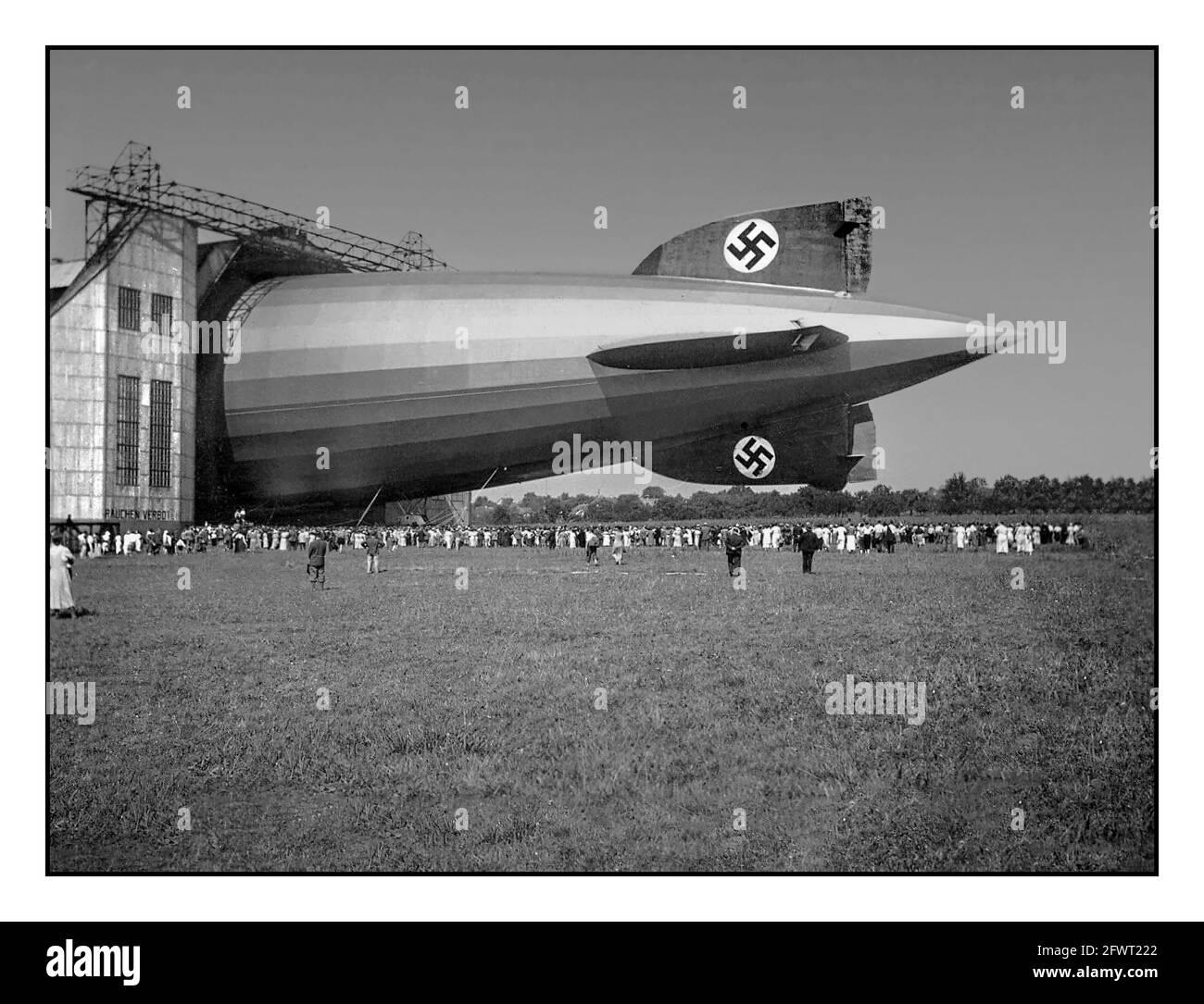 Der Graf Zeppelin, Friedrichshafen, Deutschland, 1936. „das Nazi-Monster“ ein riesiges Luftschiff mit Hakenkreuzschwanzflossen-Emblemen, das halb aus einem Hangar in Friedrichshafen ausgestellt wurde, mit Massen von Besuchern, die die neue Reisetechnologie Nazi-Deutschland der 30er Jahre beobachten konnten Stockfoto