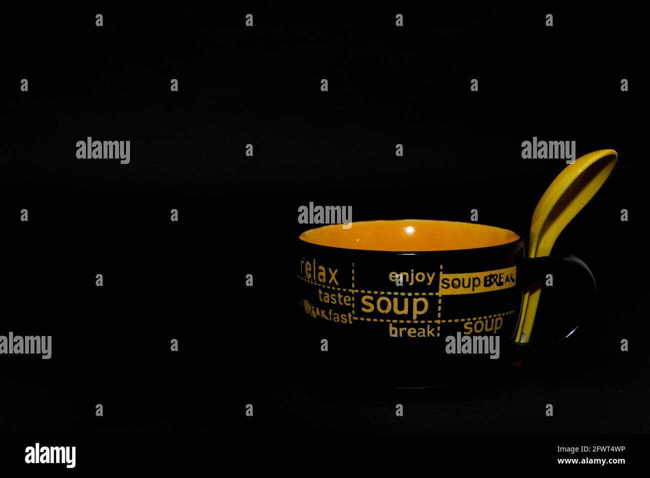 Eine keramische Suppenschüssel oder Suppenbecher mit Griff und einem gelben Löffel und einem flachen schwarzen Hintergrund Stockfoto