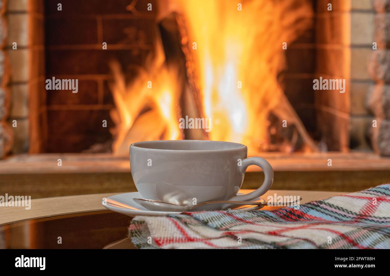 Gemütliche Kamin-Szene, weiße Tasse Tee, warmer Schal auf einem Tisch. Stockfoto