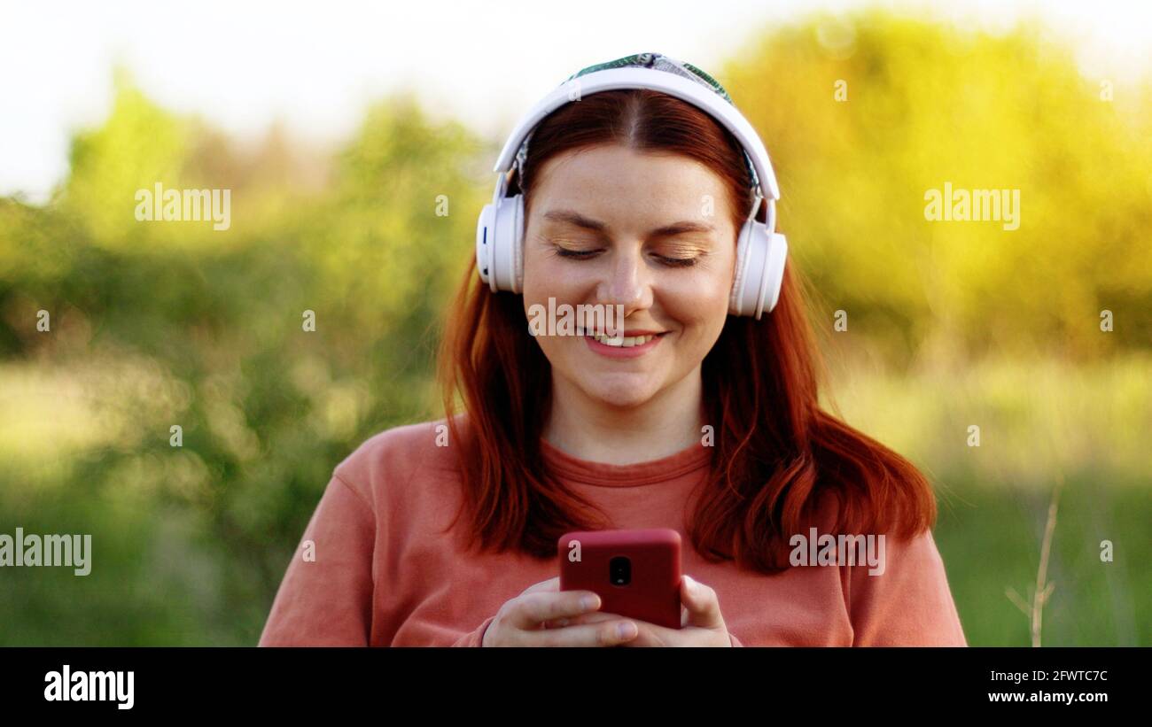 Junge Frau, die an sonnigen Tagen mit dem Smartphone Musik hört Stockfoto