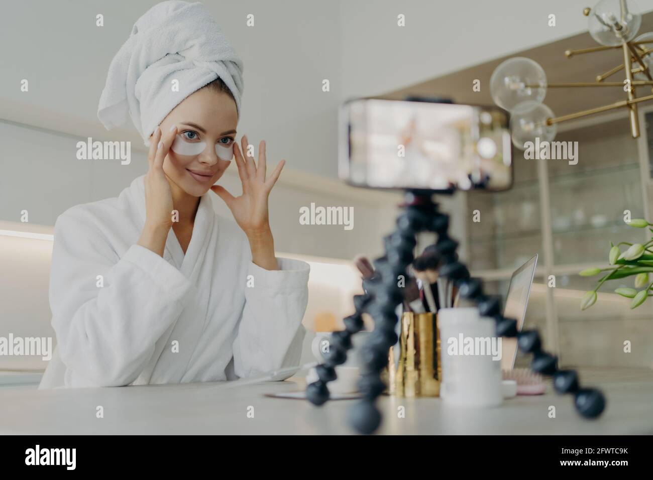 Weibliche Beauty-Bloggerin im Bademantel mit kosmetischen Patches während der Aufnahme Video über die Hautpflege für ihren Vlog Stockfoto