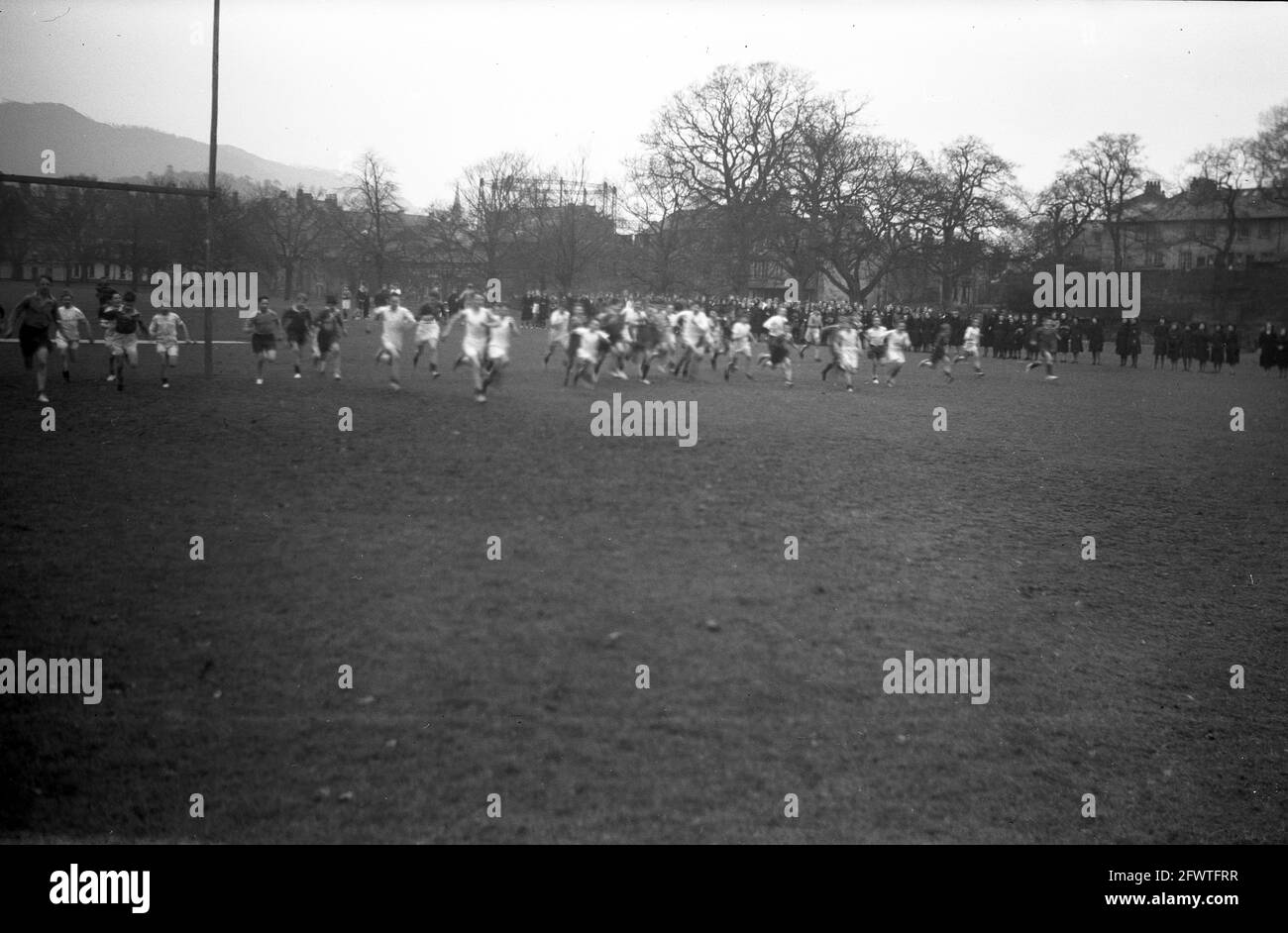 1951, historisch, in einer Reihe, eine große Gruppe von Schülern, die über einen Sportplatz Rennen, von anderen Mitgliedern der Schule beobachtet. Stockfoto