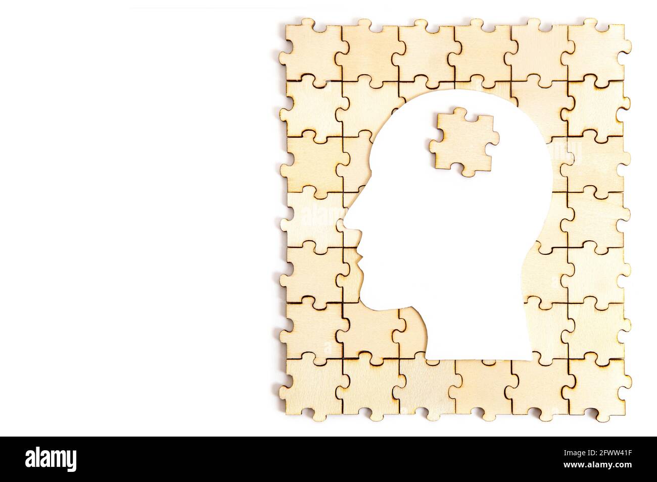 Menschlicher Kopf geformte Papiersilhouette mit einem Puzzleteil auf Oben auf einem hölzernen Puzzle isoliert auf weiß Stockfoto