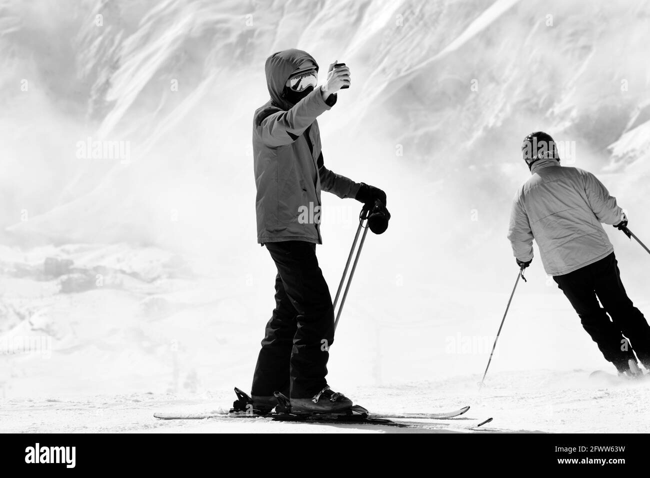 Skifahrer macht Selfie auf Kameratelefon und Schneeberge im Nebel im Hintergrund. Kaukasus im Winter, Georgien, Region Gudauri. Schwarze und weiße Tonne Stockfoto
