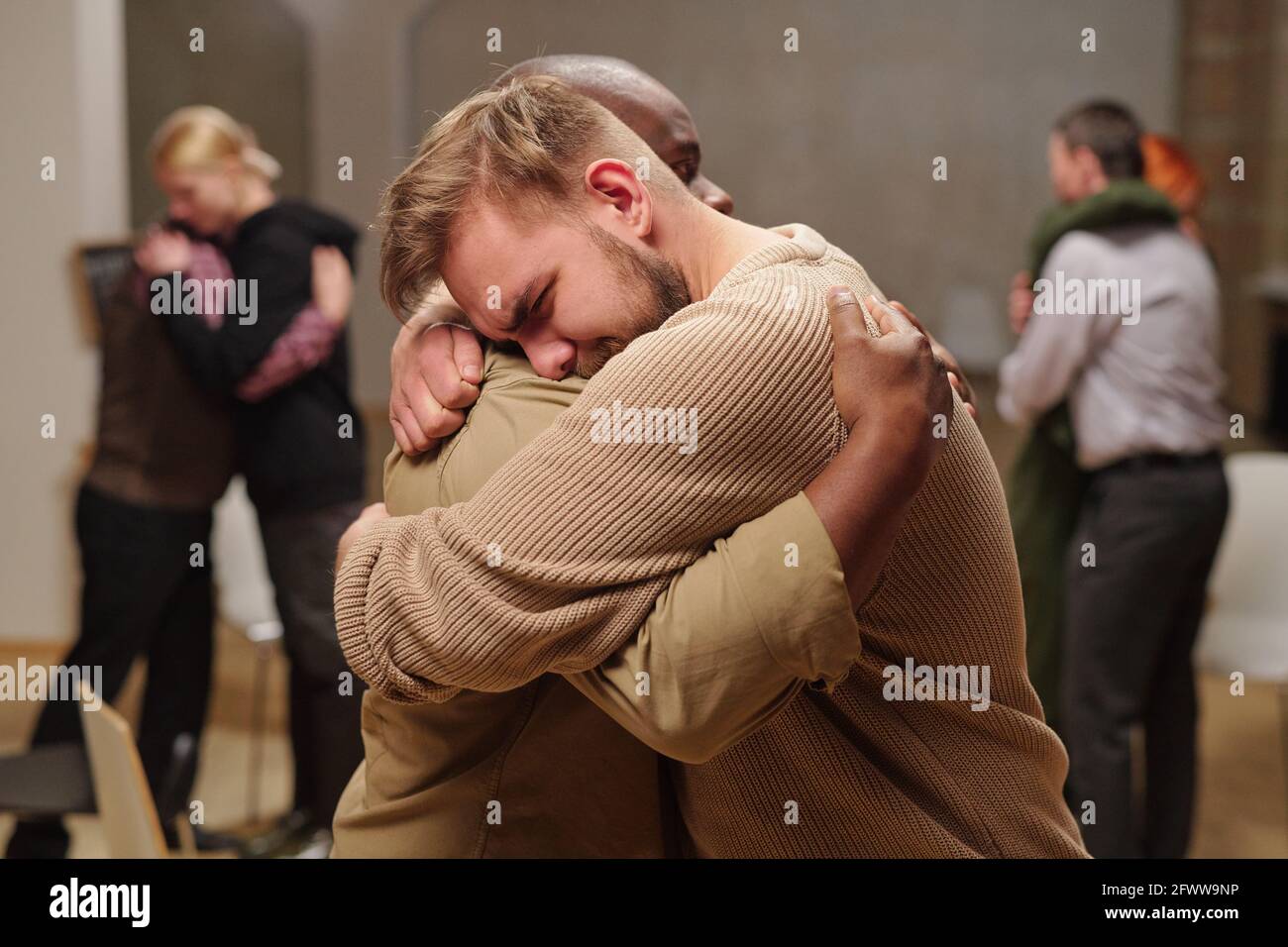 Zwei junge interkulturelle Männer umarmen sich, während einer von ihnen weint Stockfoto