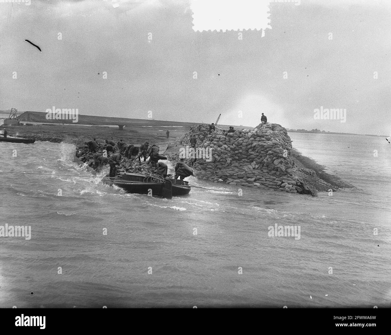 Flood 1953&#x5d; das Deichloch bei Herkingen auf Goeree-Overflakkee, das Anfang Februar 1953 gemacht wurde, aber nicht rechtzeitig geschlossen wurde, wird jetzt mit Basaltblöcken geschlossen. Dachbohnen mit diesen Blöcken werden in das Loch gesegelt und mit großer Geschwindigkeit werden die Basaltstücke dann ins Wasser geworfen., 12. März 1953, Reparaturarbeiten, Überschwemmungen, Niederlande, 20. Jahrhundert Presseagentur Foto, Nachrichten zu erinnern, Dokumentarfilm, historische Fotografie 1945-1990, visuelle Geschichten, Menschliche Geschichte des zwanzigsten Jahrhunderts, Momente in der Zeit festzuhalten Stockfoto