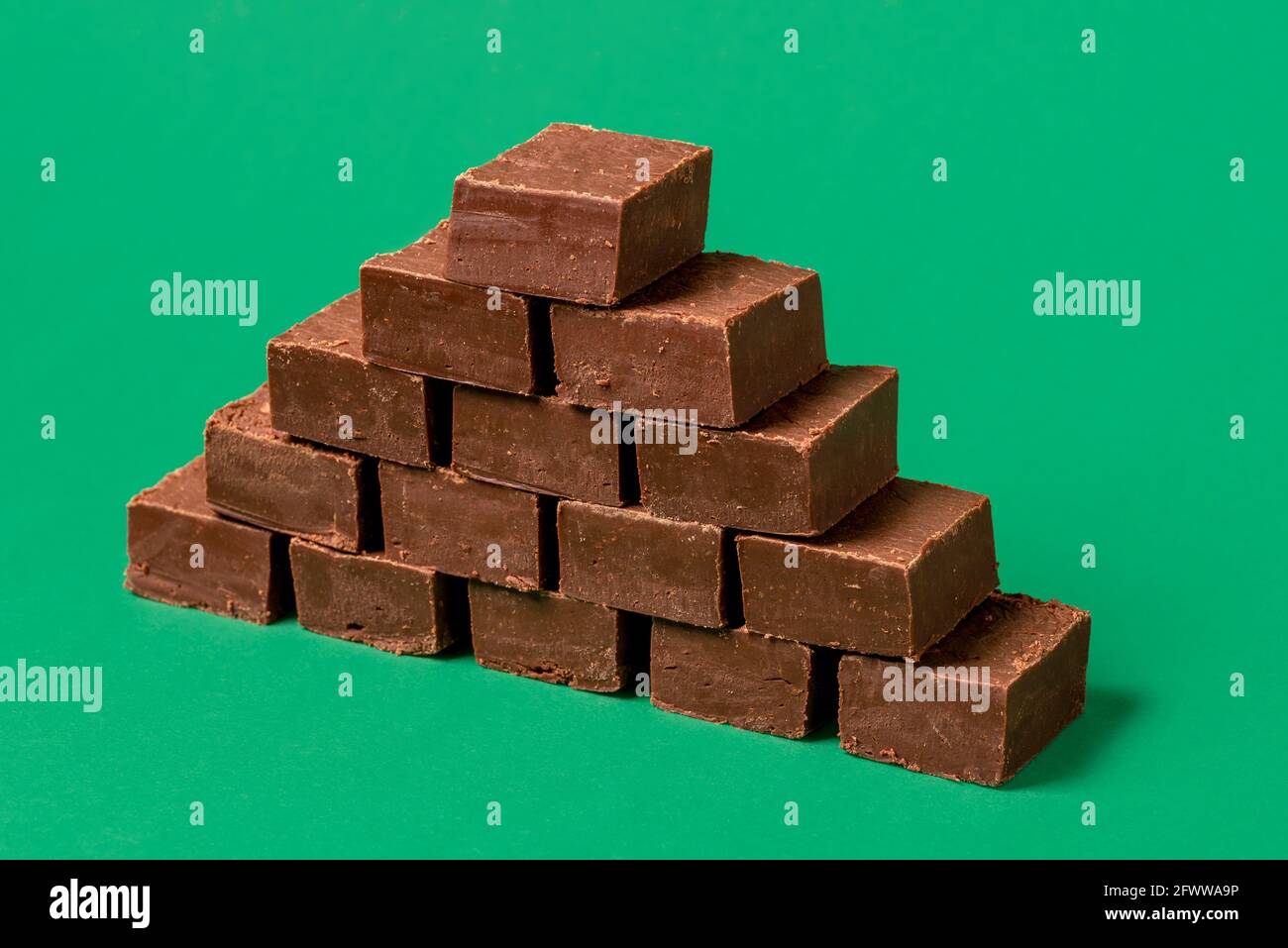 Stapel von hausgemachtem Schokoladenfondant auf einem grünen Tisch. Haufen köstlicher Schokoladen-Fudge-Riegel auf einem grünen Hintergrund isoliert. Stockfoto