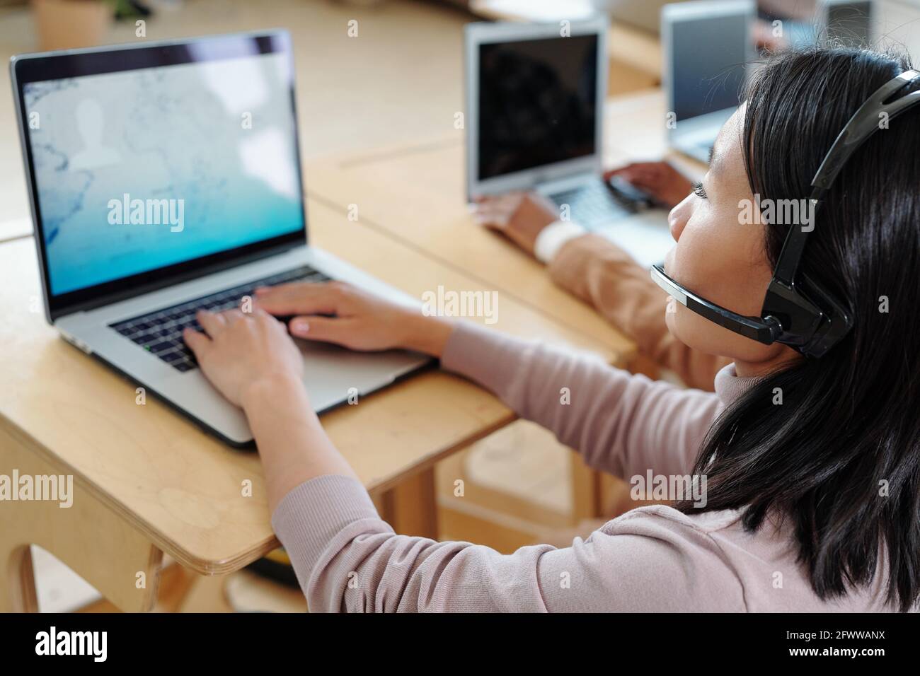 Überblicken Sie den geschäftigen jungen asiatischen Call Center-Betreiber In einem schnurlosen Headset mit Mikrofon, das den Kunden mit Informationen versorgt Notebook Stockfoto
