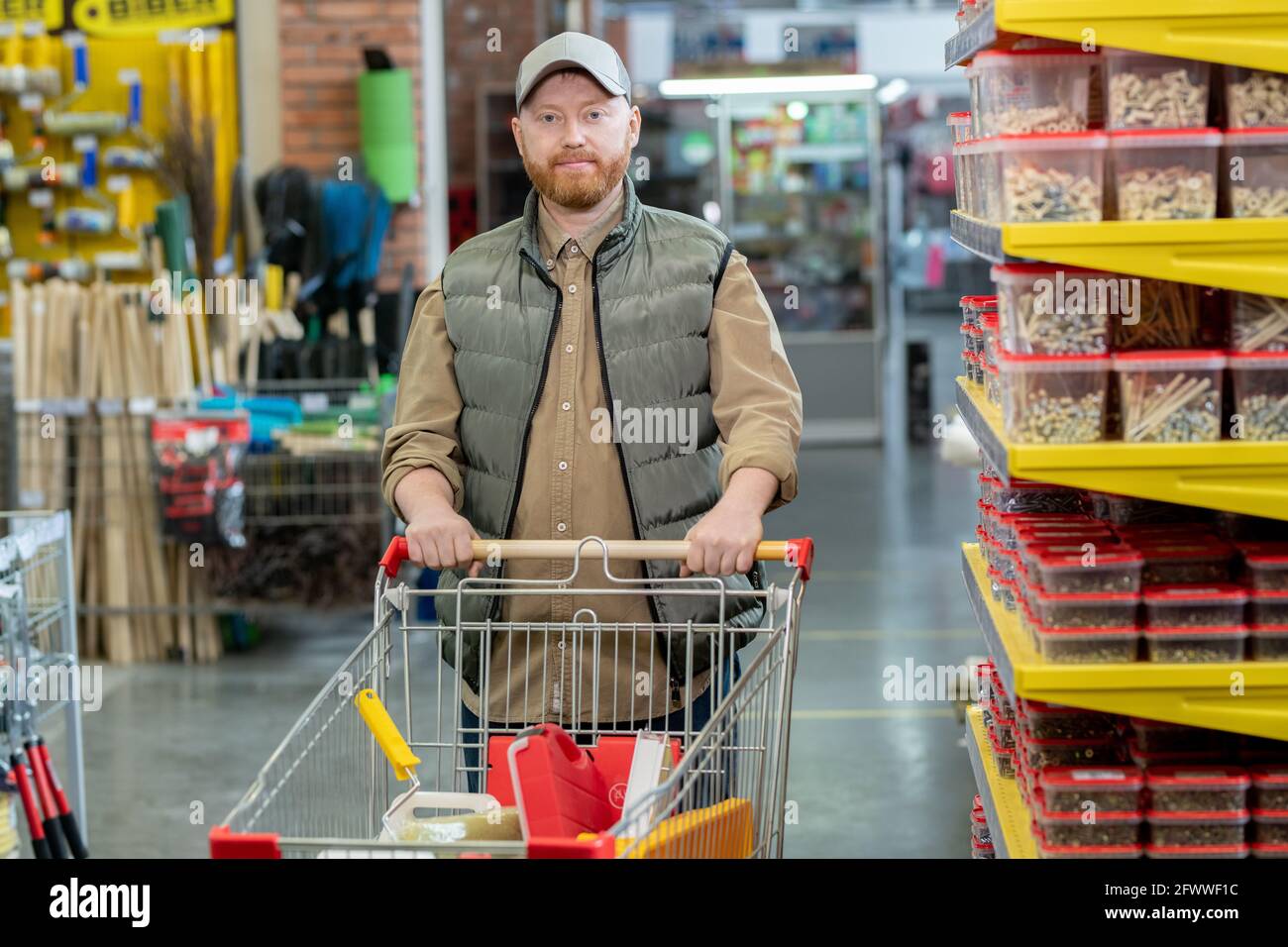 Ein glücklicher Mann mittleren Alters, der in großer moderner Einrichtung entlang der Ausstellungsflächen läuft Hardware-Supermarkt Stockfoto