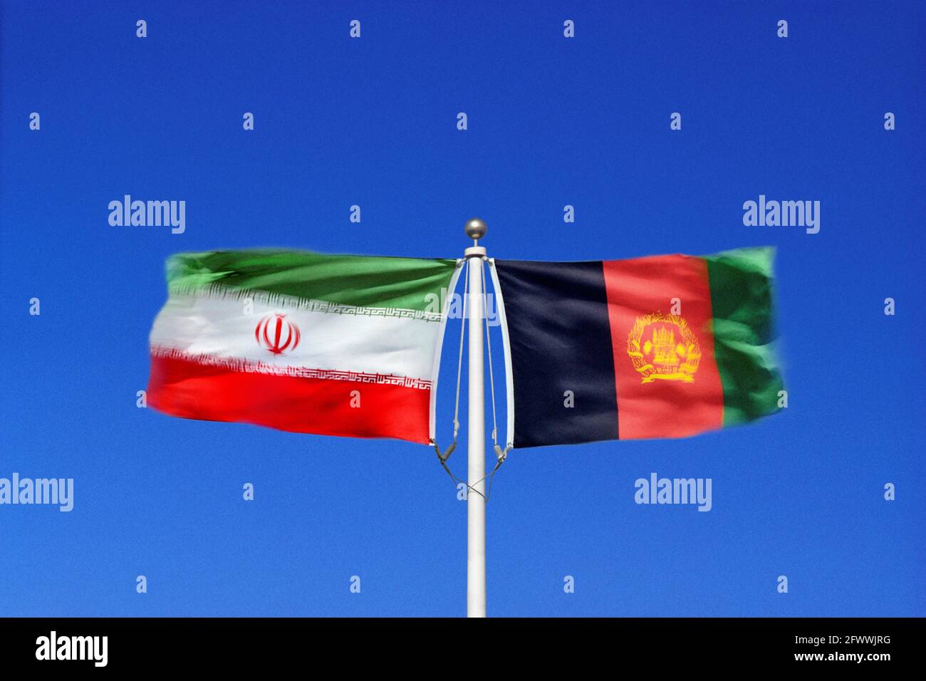Iranische und afghanische Flaggen schwingen Seite an Seite in gegenläufigen Winden auf einem einzigen Fahnenmast. Digitales Composite. Stockfoto