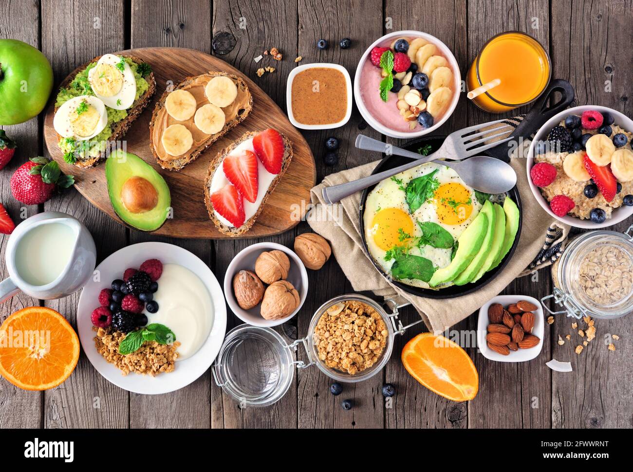 Gesunde Frühstückstisch-Szene mit Obst, Joghurt, Haferflocken, Smoothie, nahrhaftem Toast und Eierpfanne. Draufsicht über einen Holzhintergrund. Stockfoto
