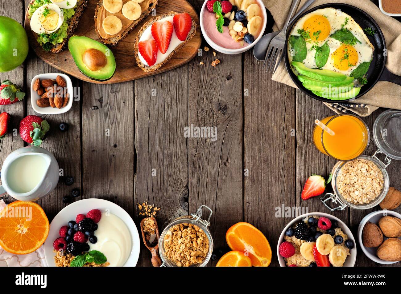 Gesunde Frühstückskost Rahmen. Tischszene mit Obst, Joghurt, Smoothie, Haferflocken, nahrhaftem Toast und Eierpfanne. Blick von oben auf einen rustikalen Holzhintergr Stockfoto