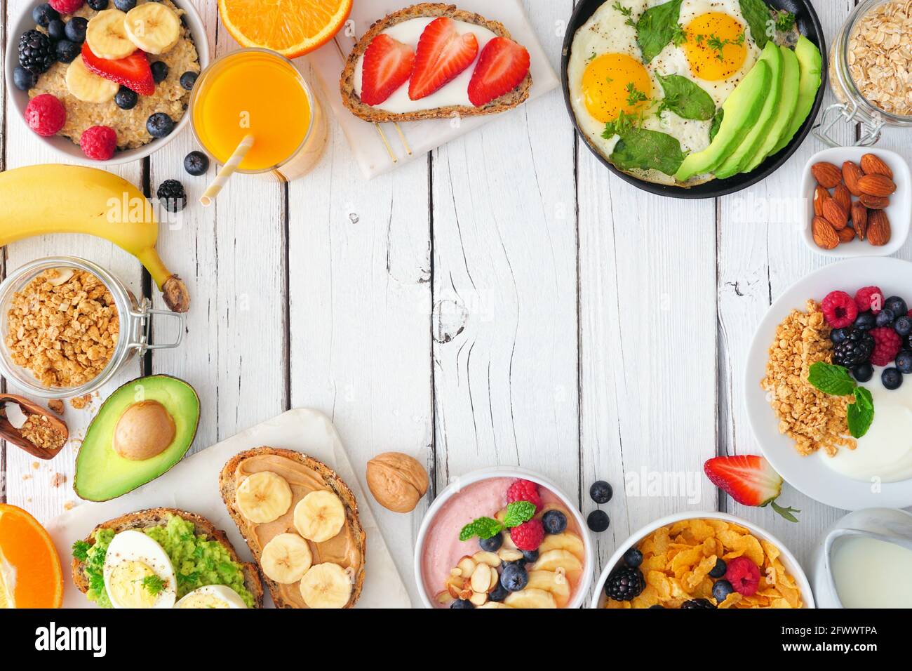 Gesunde Frühstückskost Rahmen. Tischszene mit Obst, Joghurt, Smoothie, Haferflocken, nahrhaftem Toast und Eierpfanne. Blick von oben auf eine weiße Holz-BA Stockfoto