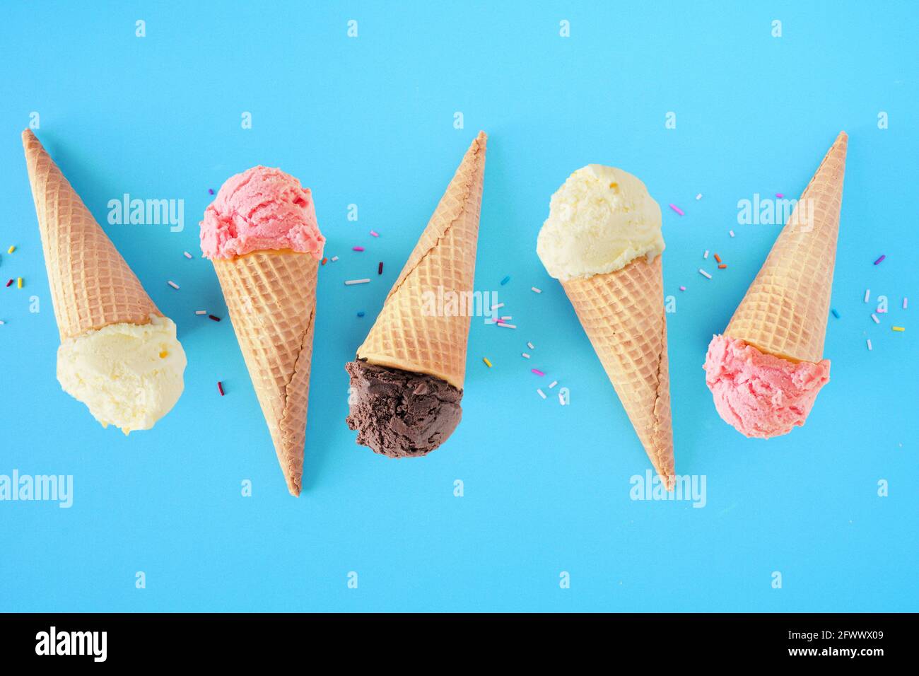 Eiskonus flach auf blauem Hintergrund. Aromen von weißer Vanille, rosa Erdbeere und dunkler Schokolade. Stockfoto