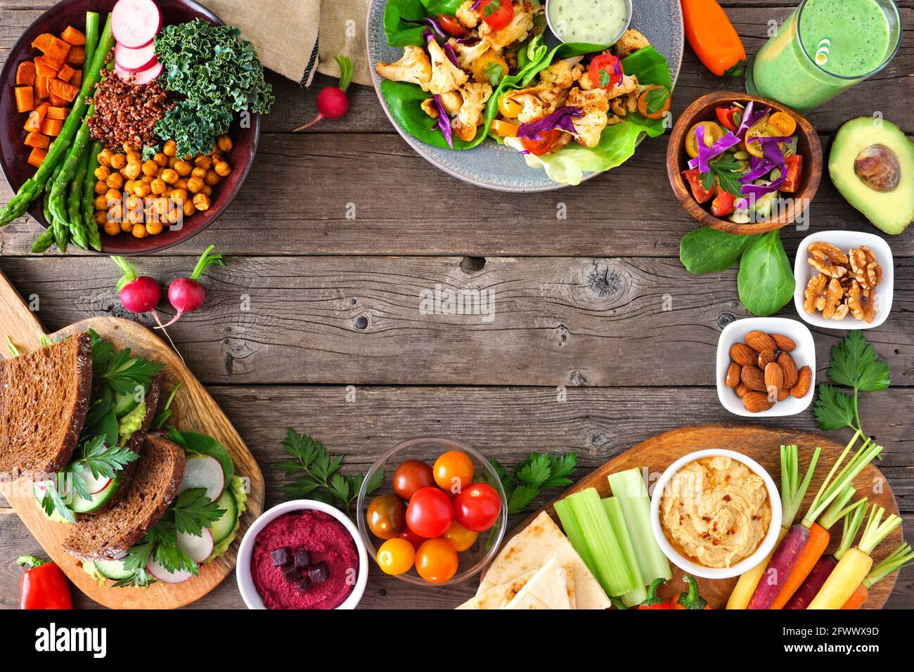 Gesundes Essen Rahmen. Tischszene mit nahrhafter Buddha-Schüssel, Salatpackungen, Sandwiches, Salat und Gemüse. Blick von oben auf ein rustikales Holz b Stockfoto