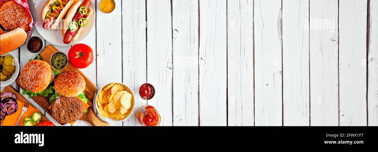 Sommer BBQ Food Tischszene mit Hot Dog und Hamburger Buffet. Über Ansicht Eckrand über einem weißen Holz Banner Hintergrund. Speicherplatz kopieren. Stockfoto