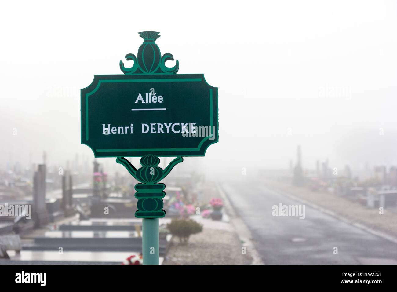 Schild mit der Bezeichnung „Henri DERYCKE Alley“ mit Gräbern und Kreuzen im Hintergrund im Nebel auf dem Friedhof Saint roch. Stockfoto