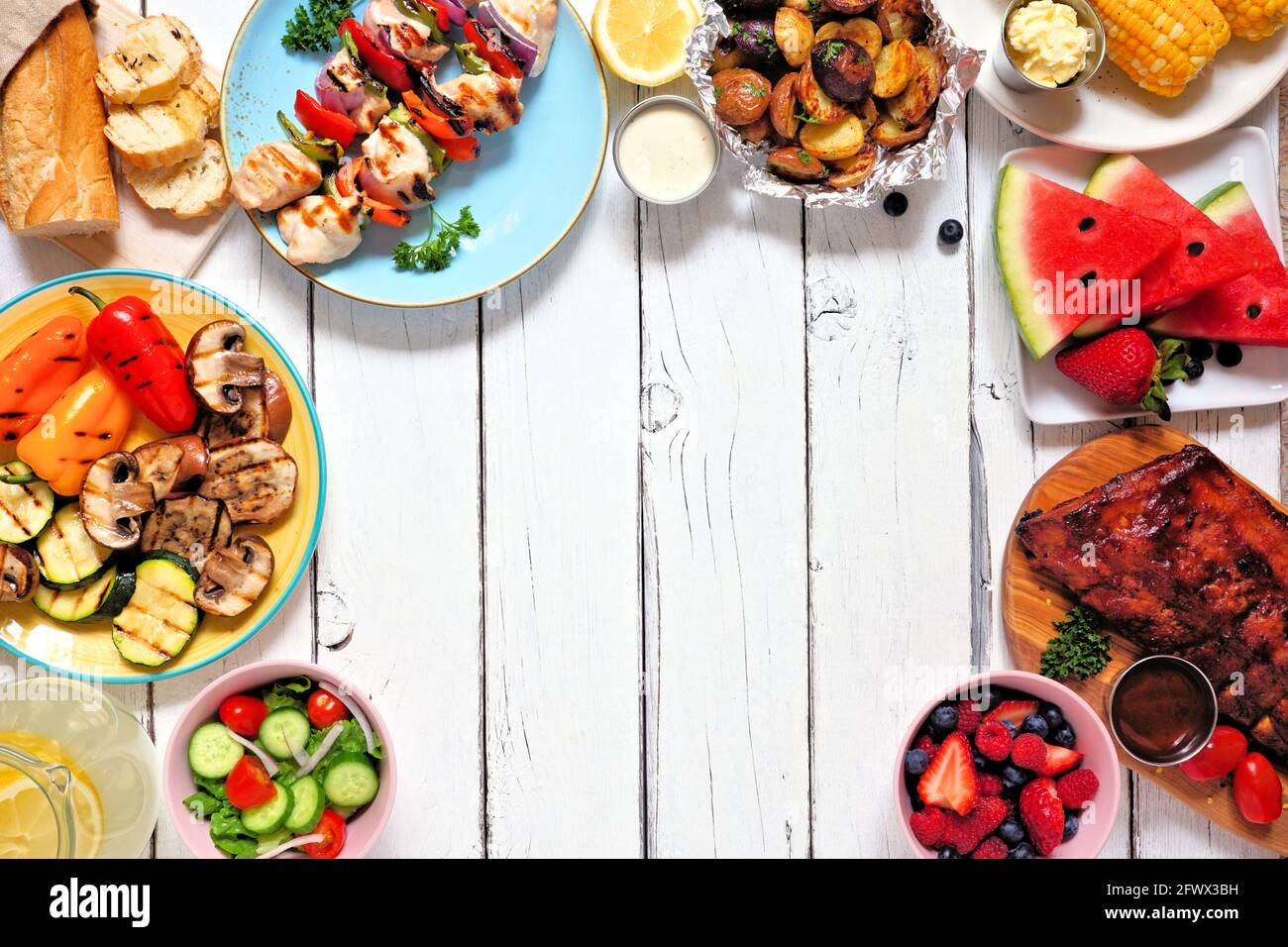 Sommer BBQ oder Picknick-Rahmen. Auswahl an gegrilltem Fleisch, Gemüse, Obst, Salat und Kartoffeln. Blick über einen weißen Holzhintergrund. Speicherplatz kopieren Stockfoto
