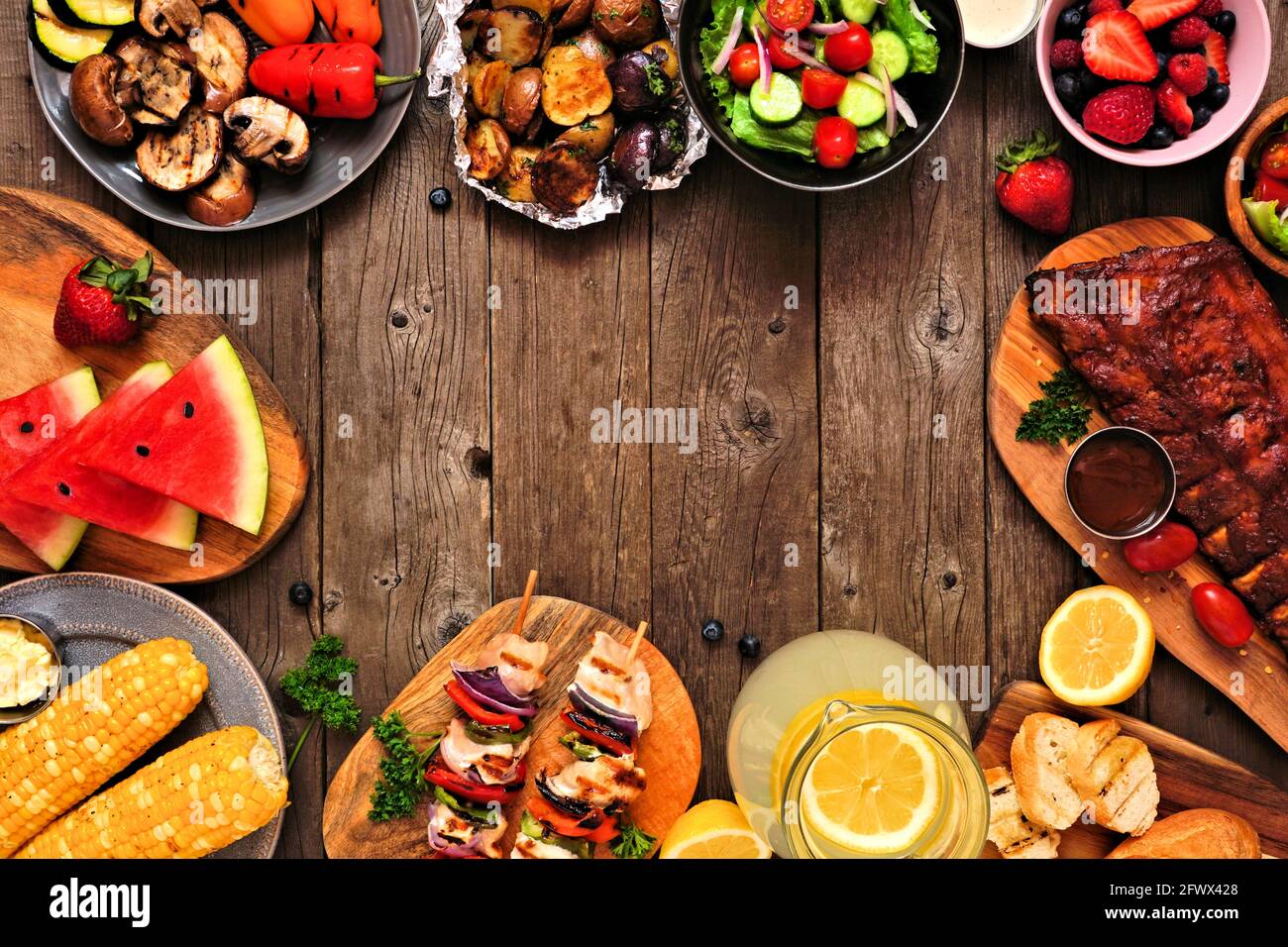 Sommer-BBQ oder Picknick-Essen Rahmen über einem rustikalen Holz Hintergrund. Auswahl an gegrilltem Fleisch, Gemüse, Obst, Salat und Kartoffeln. Draufsicht mit Stockfoto