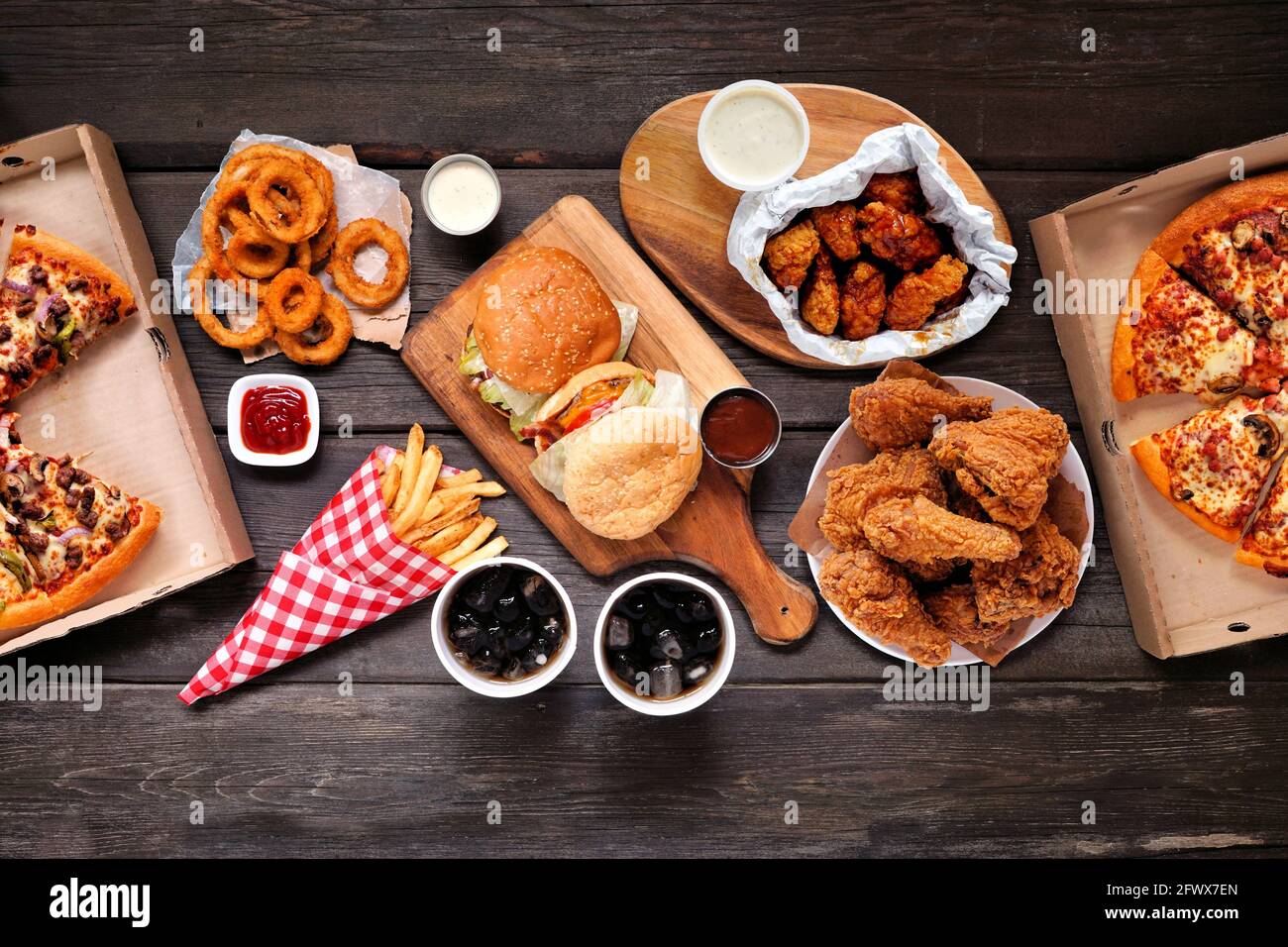 Tischszene mit großer Auswahl an Take-Out- und Fast-Food-Gerichten. Hamburger, Pizza, gebratenes Huhn und Beilagen. Oben auf einem dunklen Holzhintergrund. Stockfoto