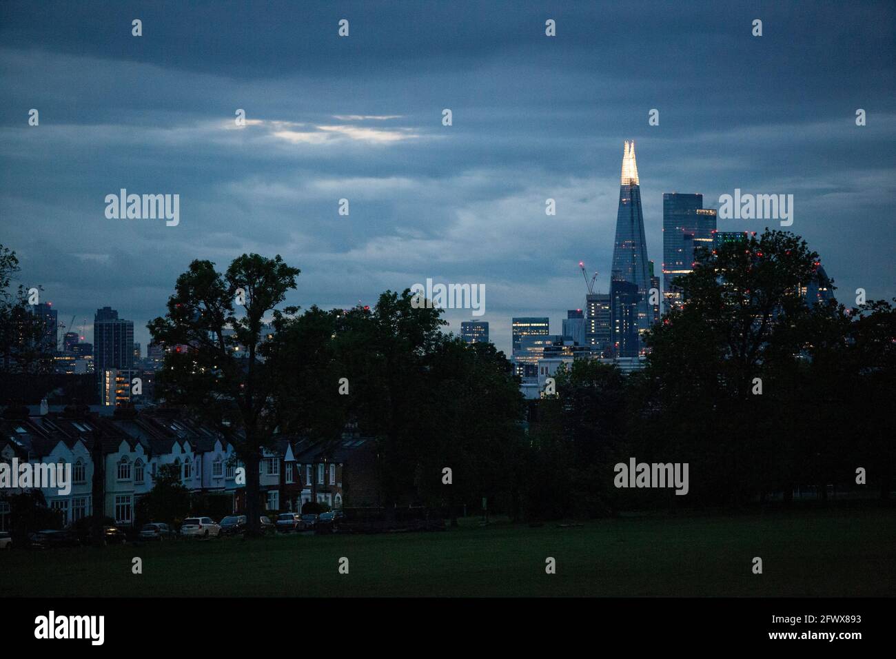 UK Weather, London, 24 May 2021: In der Abenddämmerung sorgt das stürmische Wetter mit starken Regenschauern für eine dramatische Skyline mit den Lichtern im Zentrum Londons, die im Kontrast zu den Vorstadthäusern stehen, die den Ruskin Park von Camberwell säumen. AnnaWatson/Alamy Live News Stockfoto