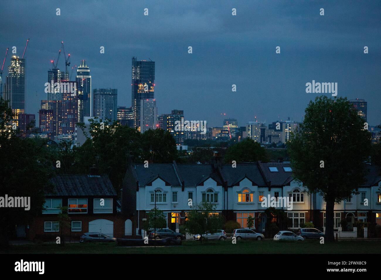 UK Weather, London, 24 May 2021: In der Abenddämmerung sorgt das stürmische Wetter mit starken Regenschauern für eine dramatische Skyline mit den Lichtern im Zentrum Londons, die im Kontrast zu den Vorstadthäusern stehen, die den Ruskin Park von Camberwell säumen. AnnaWatson/Alamy Live News Stockfoto