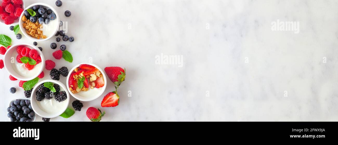 Gesunde Joghurtschüsseln mit verschiedenen Beeren und Müsli. Banner mit Eckrand auf weißem Marmorgrund. Speicherplatz kopieren. Stockfoto
