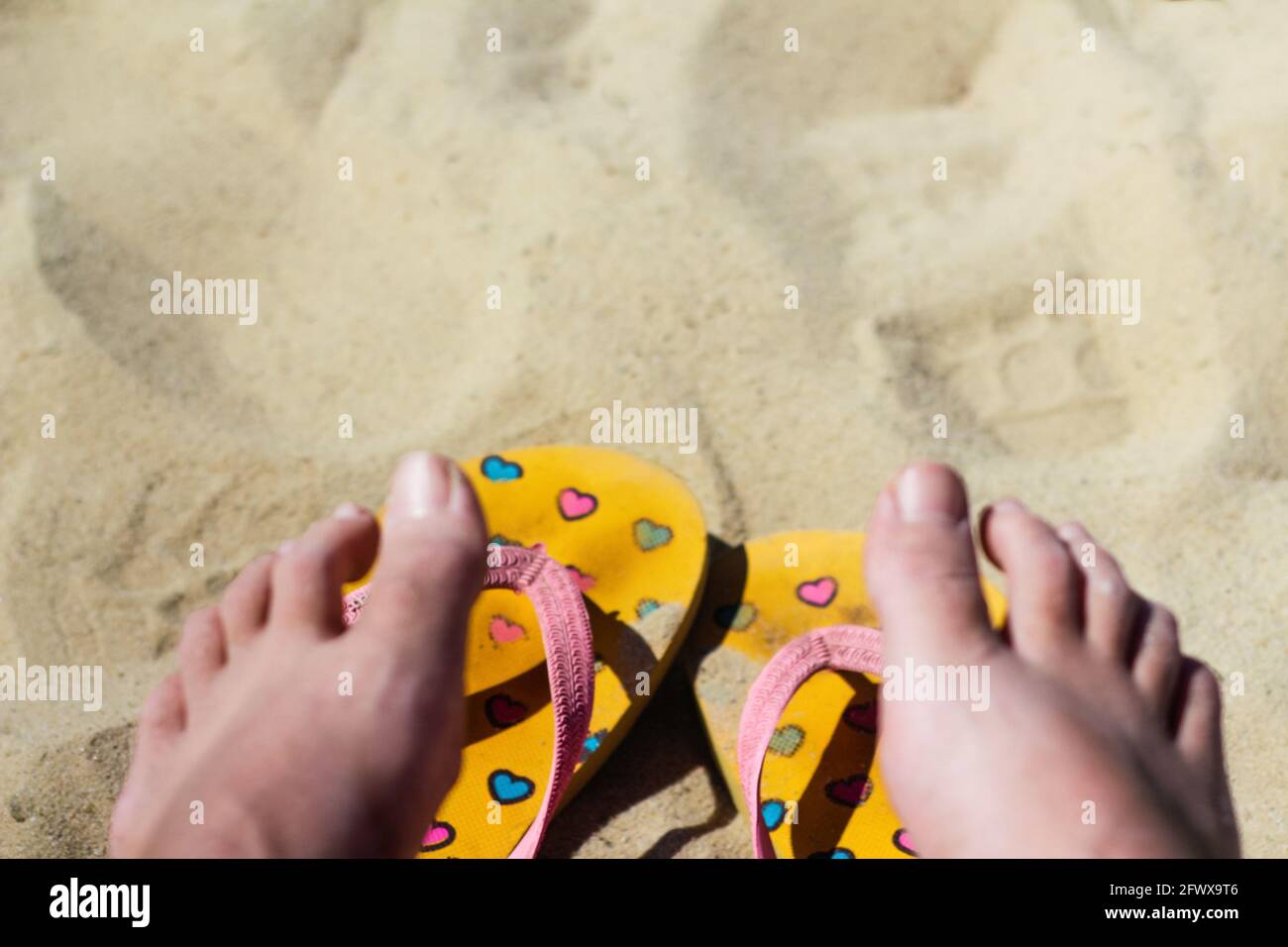 Unschärfe schmutzige helle gelbe und rosa Hausschuhe Flip Flops mit Herzen auf dem Sand. Verschwommene weibliche Heldentat. Sommer Hintergrund.das Konzept der Wärme, relaxati Stockfoto