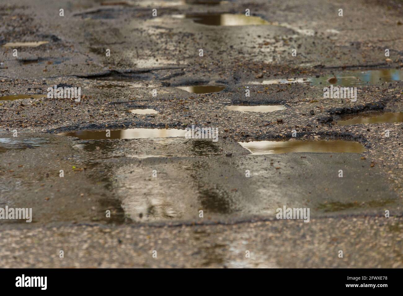 Schlaglöcher und Pfützen auf schlecht gebrochener nasser Asphaltstraße danach Rain – Vollformathintergrund Stockfoto