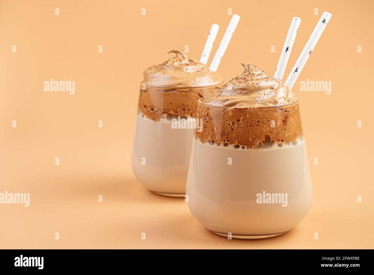 Dalgona-Kaffee-Nahaufnahme in zwei klaren Gläsern mit Trinkhalmen auf orangefarbenem Hintergrund. Stockfoto