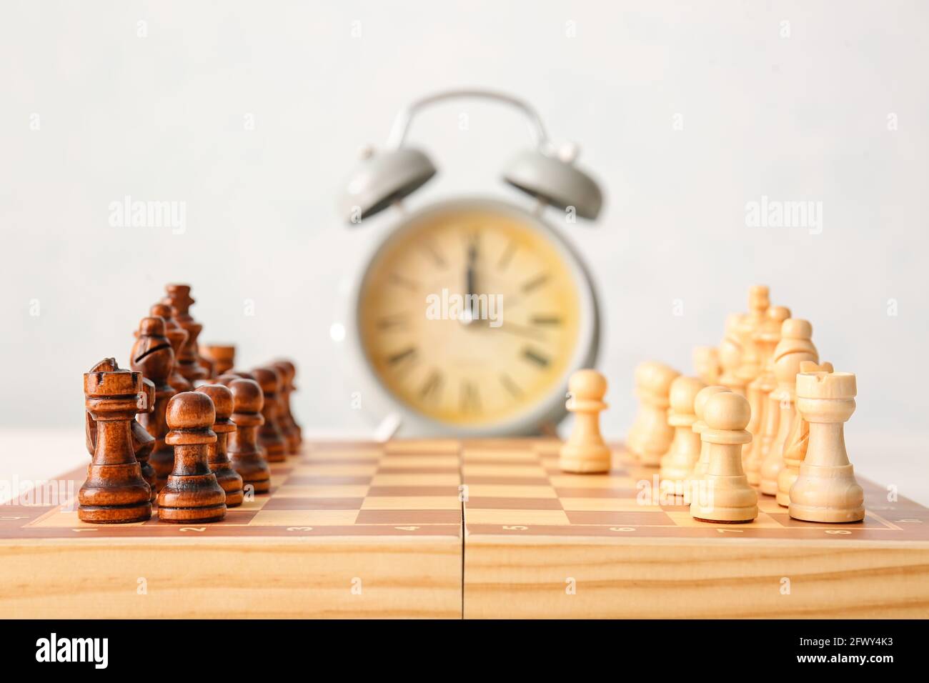 Schachbrett und Wecker auf weißem Hintergrund Stockfoto