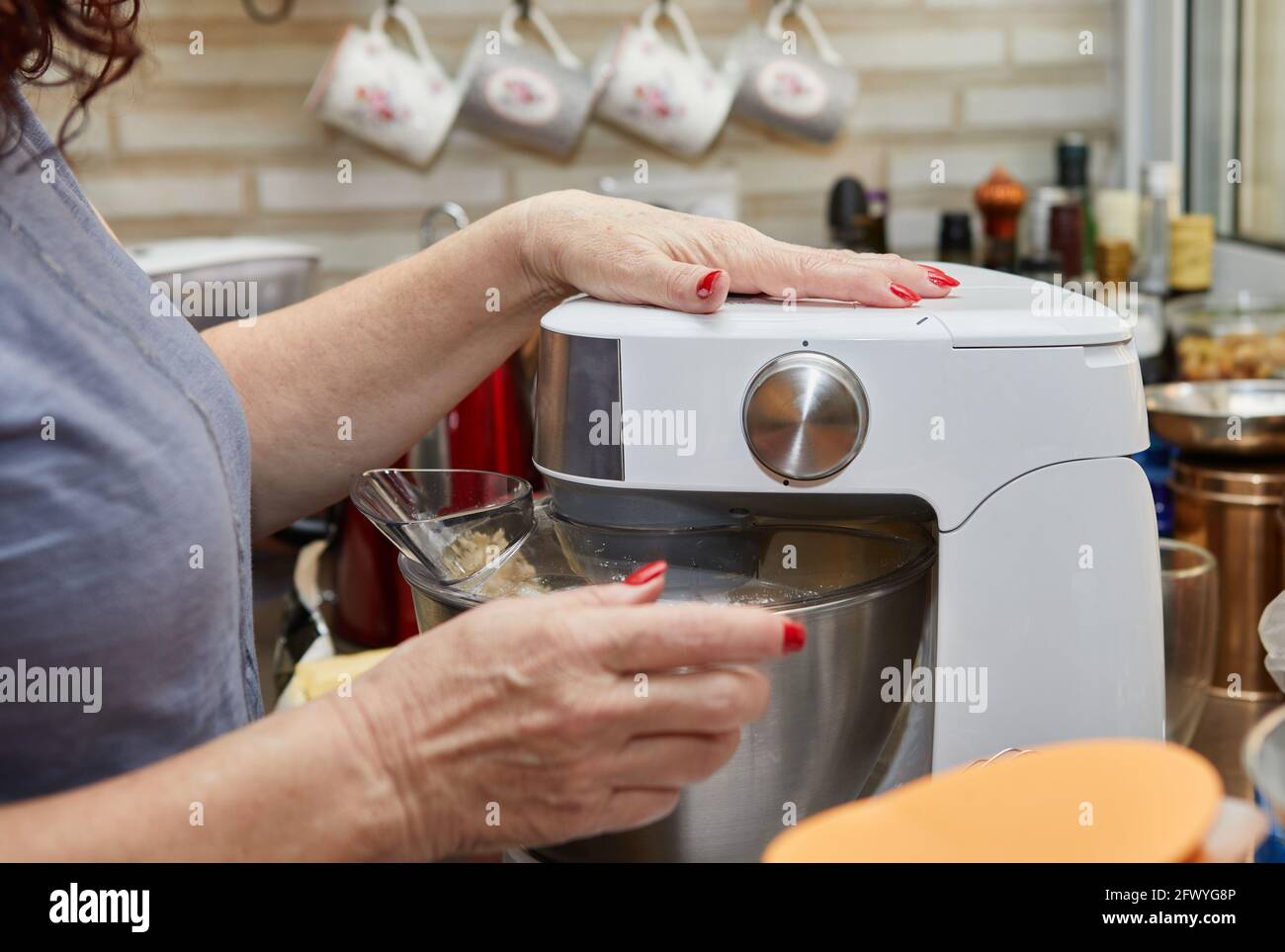 Frau schlägt den Teig mit einem Mixer, um Muffins zuzubereiten Mit getrockneten Tomaten Stockfoto