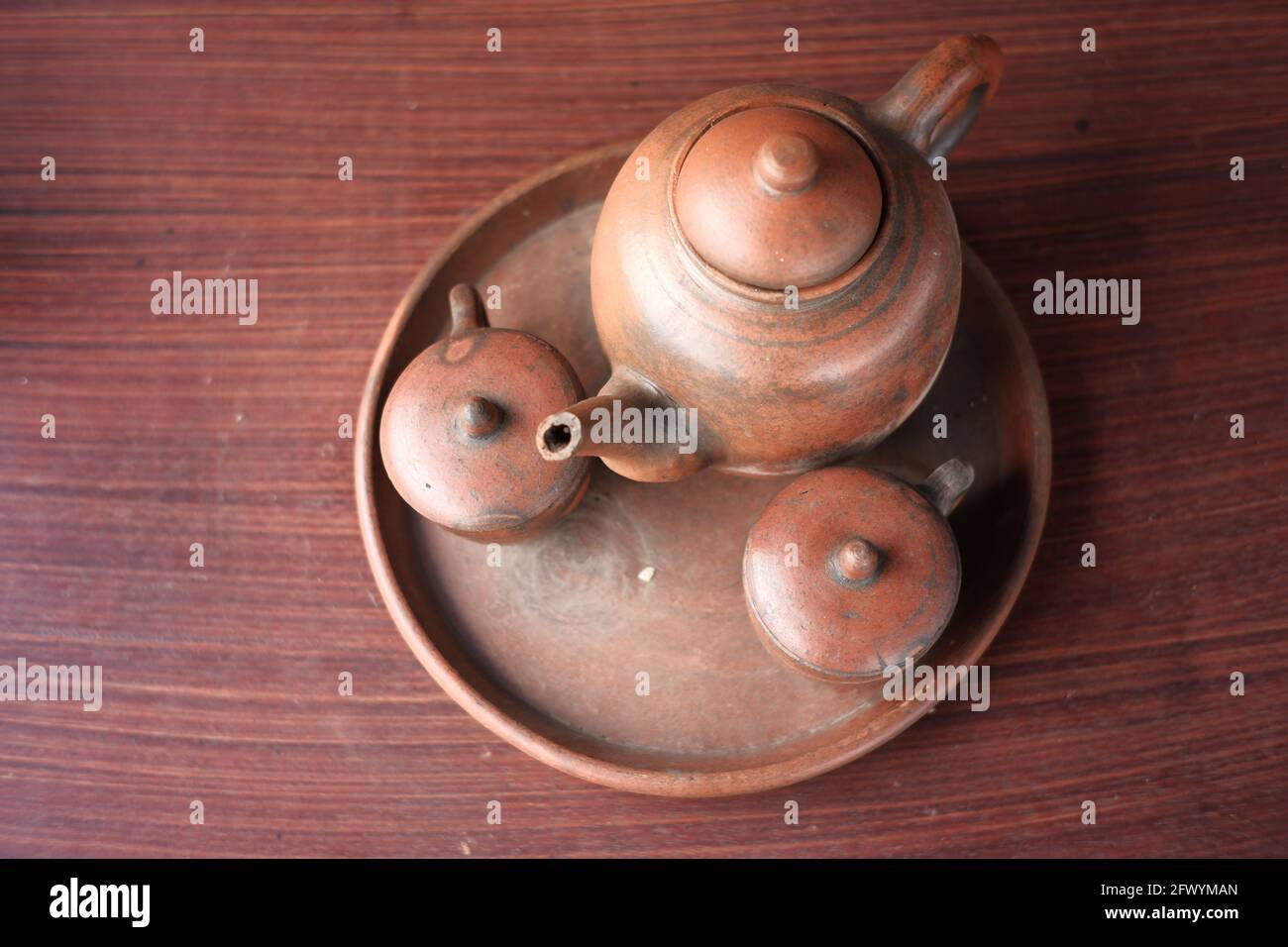 Wasserkocher und Gläser aus Ton. Traditionelle javanische Küchengeräte für warme Getränke. Indonesisches rotes Küchengeschirr auf einem hölzernen Stockfoto