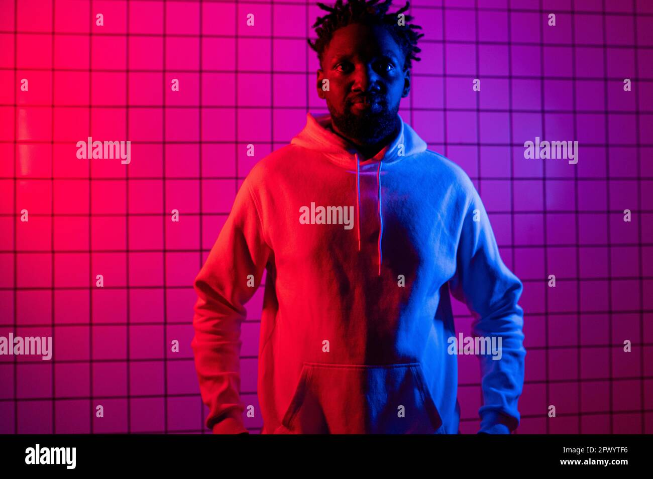 Porträt eines afroamerikanischen Mannes in einem Hoodie auf Neon-Hintergrund. Rot-blauer Hintergrund. Stockfoto
