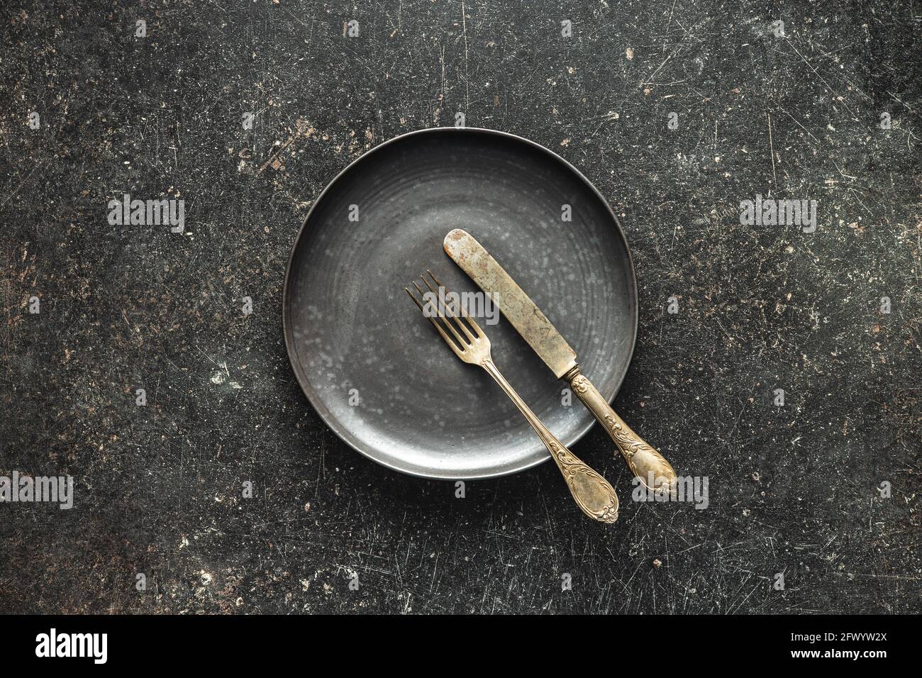 Leerer Vintage Teller mit silbernem Messer und Gabel auf schwarzem Tisch. Draufsicht. Stockfoto