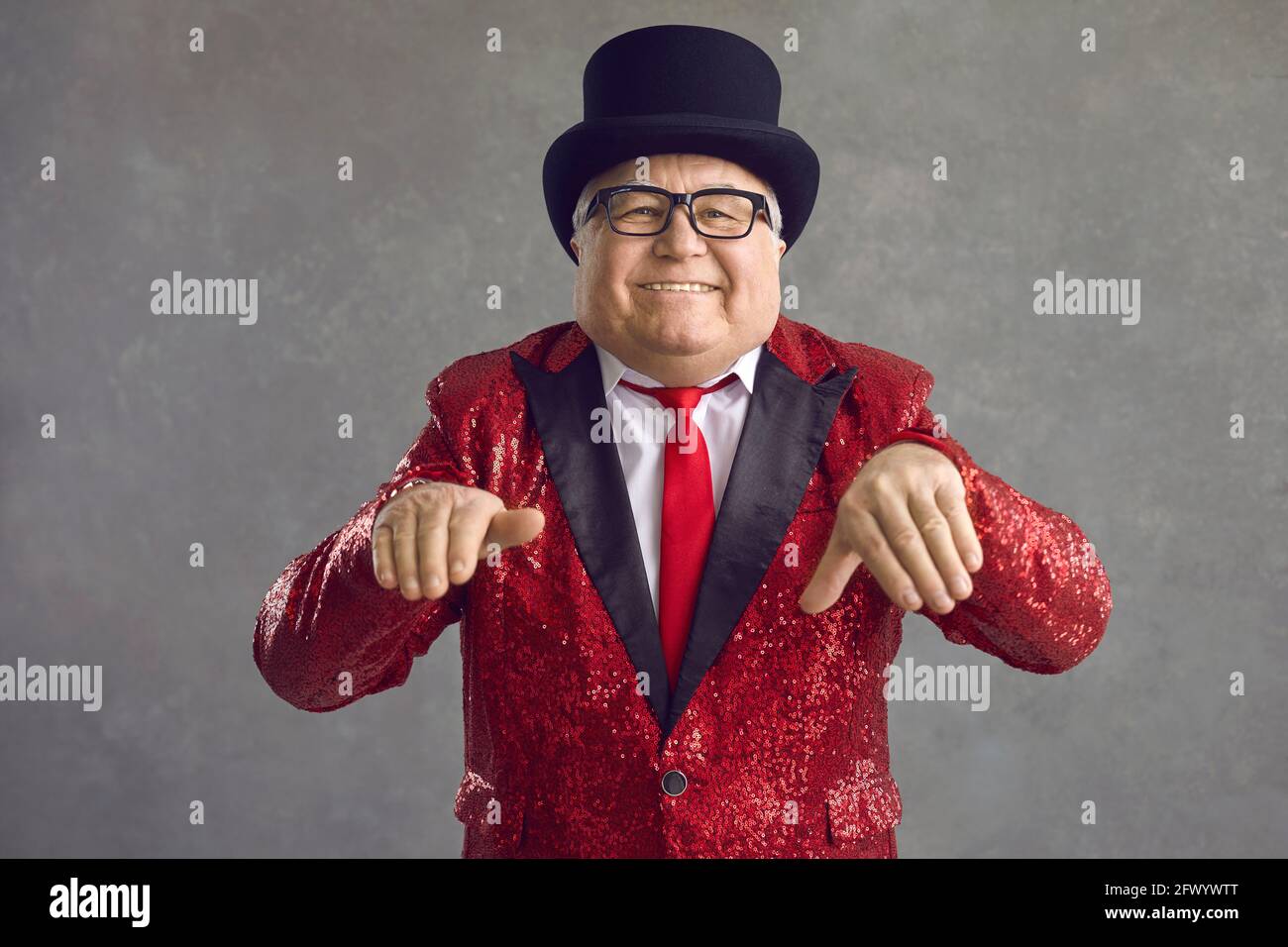 Lustiger molliger reicher älterer Mann in glänzender Jacke und schwarz Hut tanzend und lächelnd Stockfoto