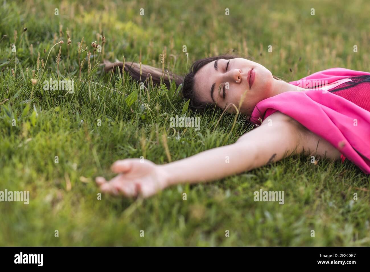 Attraktive kaukasische Frau, die mit geschlossenen Augen auf dem Gras liegt Stockfoto