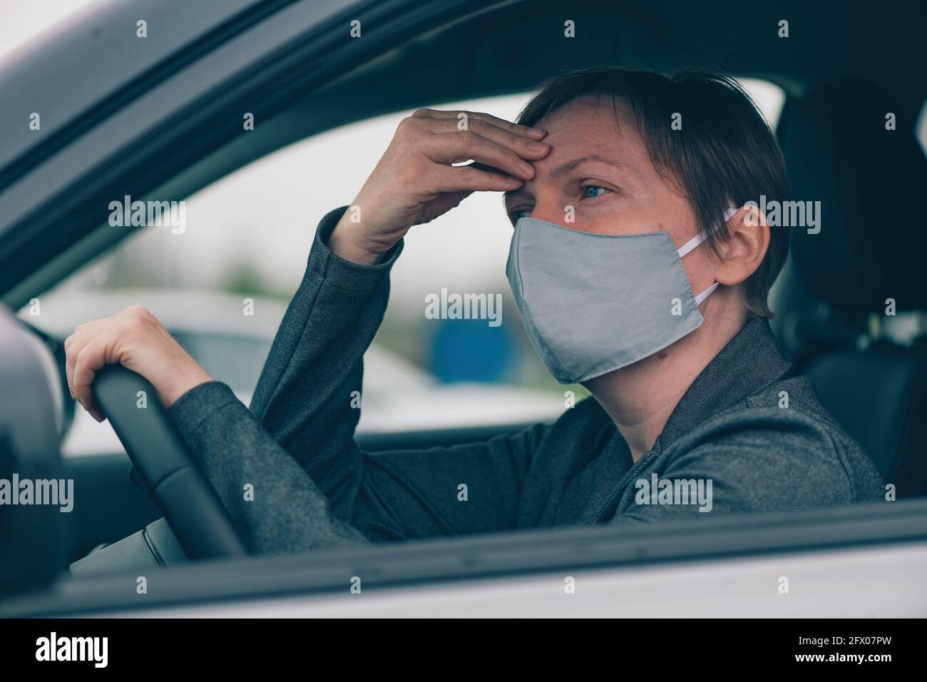 Besorgte Frau mit schützender Gesichtsmaske, die beim Warten Kopfschmerzen hat Im Auto und Blick in die Ferne Stockfoto