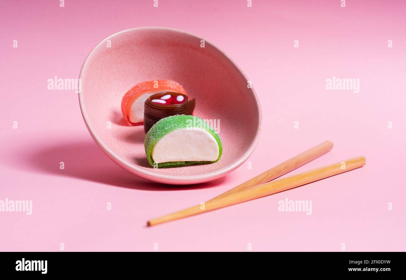 Appetitlich buntes, süßes Sushi auf Keramikplatte mit Holzplatte Essstäbchen auf rosa Hintergrund platziert Stockfoto